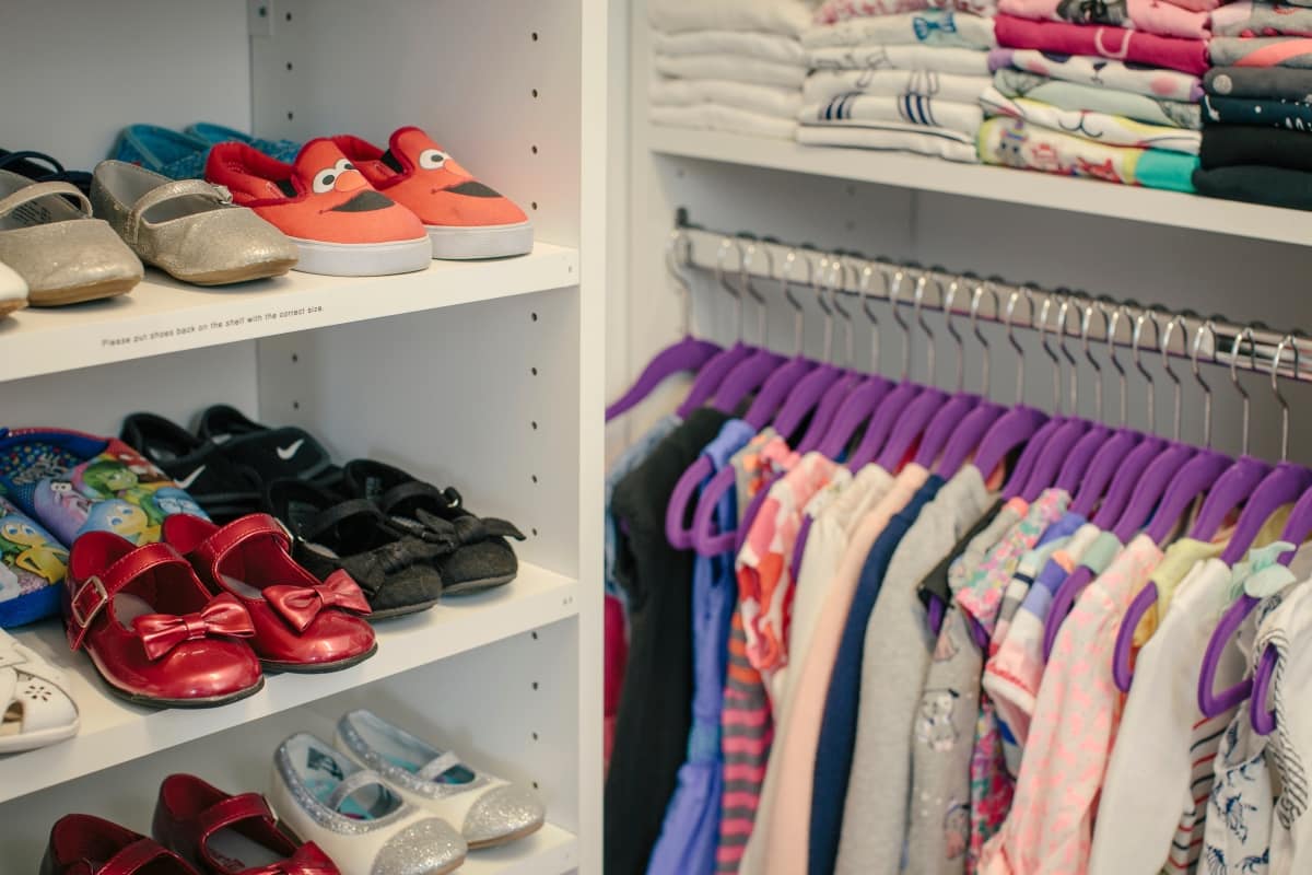 Closet up of children's shoes on shelves and clothes hung on racks and folded on shelves